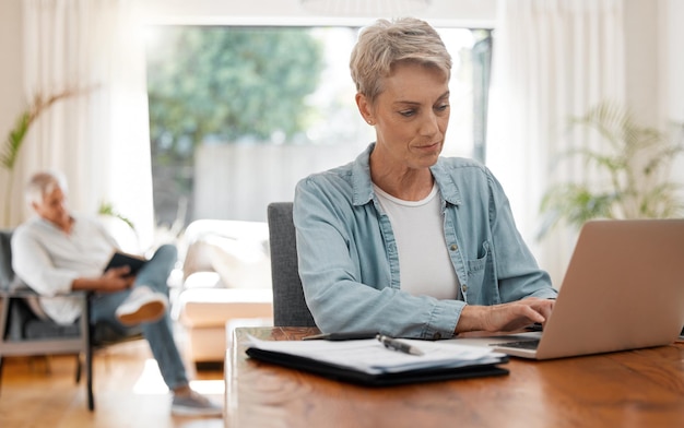 Woman on laptop doing financial budget taxes or planning monthly finance bank payment at home living room desk Lady working remote on debt solution typing on computer and husband reading a book