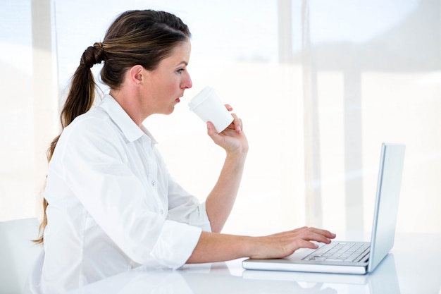 woman on a laptop drinking a coffee, at her desk