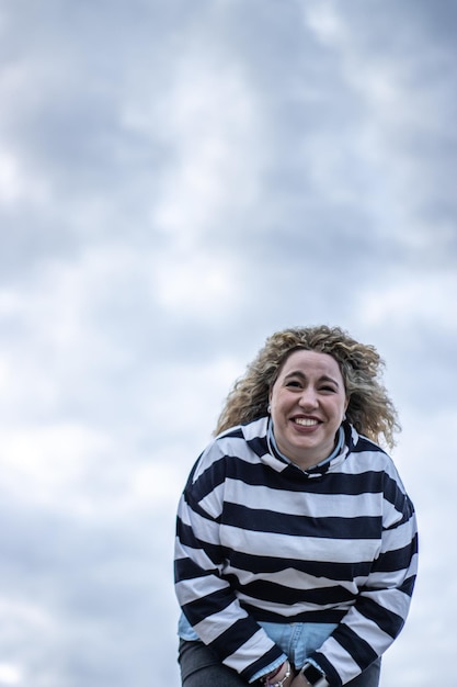 A woman laughing loudly outdoors against a background of cloudy sky