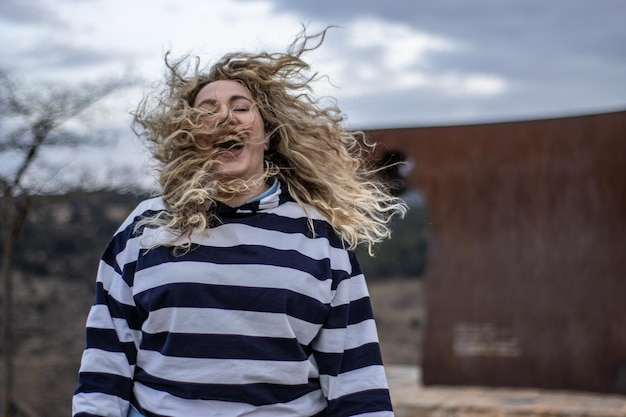 A woman laughing with her hair blowing in the wind outdoors on a cloudy day