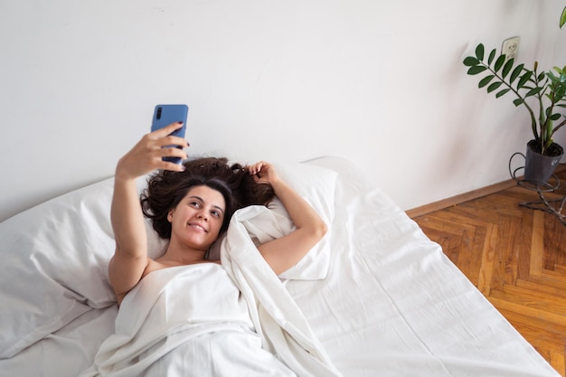 Woman laying in bed taking selfie on the phone