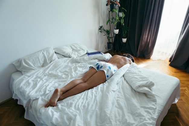 Woman laying on the bed white sheets light from window with curtains