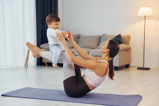 Woman laying down on mat and holding little girl Mother with her little daughter is at home together