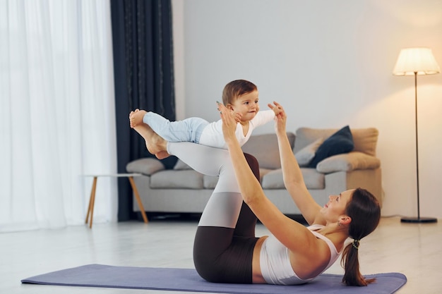 Woman laying down on mat and holding little girl Mother with her little daughter is at home together