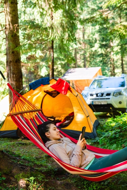 Woman laying in the hammock tent and car on background reading book