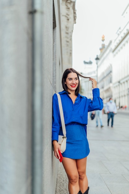 Woman leans against a wall with a phone in hand