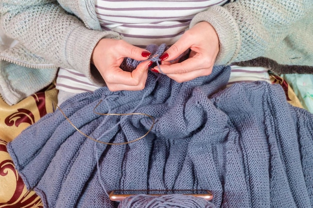 woman learns to knit looking at her smartphone, closeup