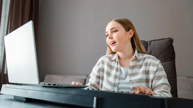 Woman learns music singing vocals playing piano online using laptop at home interior Teenager girl sings song play piano synthesizer during video call online lesson with teacher Long web banner