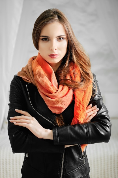 Woman in leather jacket and silk scarf over her neck standing with crossed arms