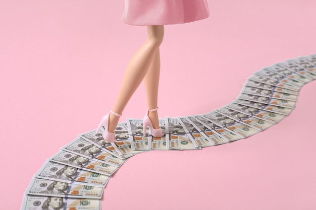 Woman legs walk along a money path, dollar bills road on pink background.