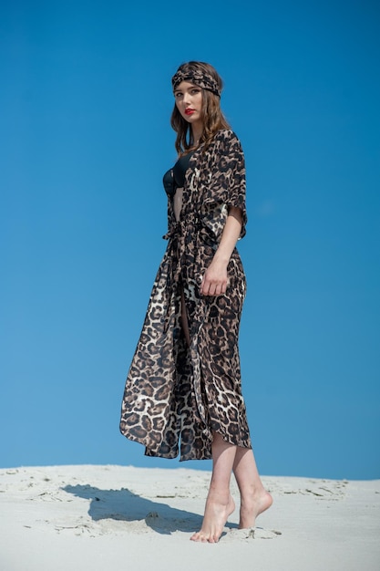 A woman in a leopard print coat stands on a hill in front of a blue sky.