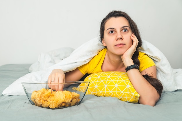 Woman lie on the bad watch movie and eat snaks