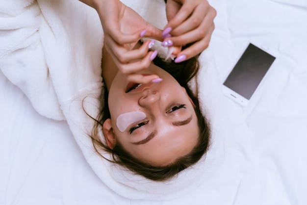 Photo woman lies on the bed and puts under the eyes patches