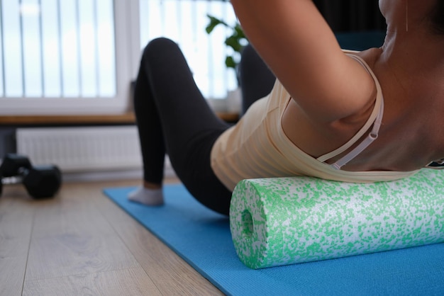 A woman lies on a sports roller does exercises for the back