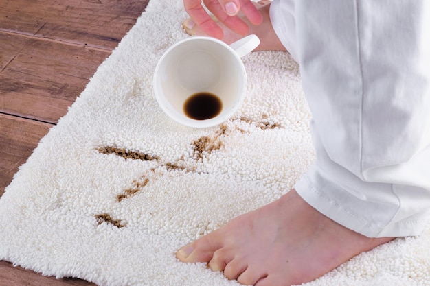 A woman lifting a cup with spilled coffee onto a carpet. Domestic failure. daily life stain concept