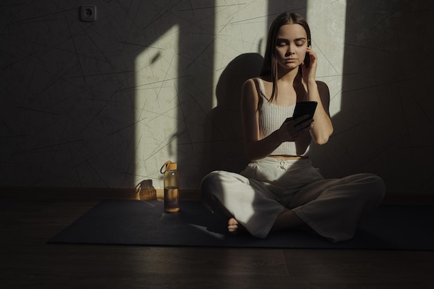 woman listening to meditation music in earbuds via smartphone while sitting in Lotus pose