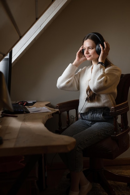 Woman listening to music in big headphones near computer