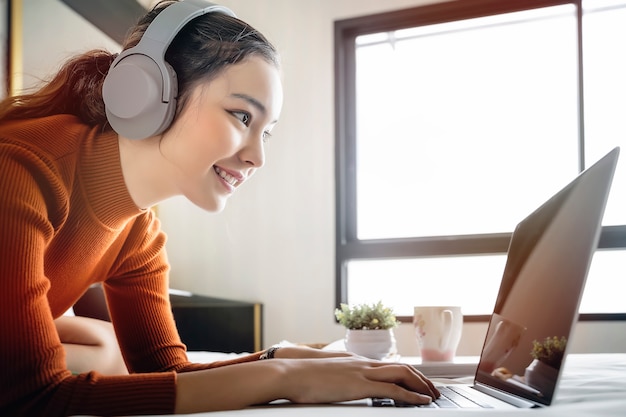 Woman listening to music with headphones and using laptop computer while relaxing at home