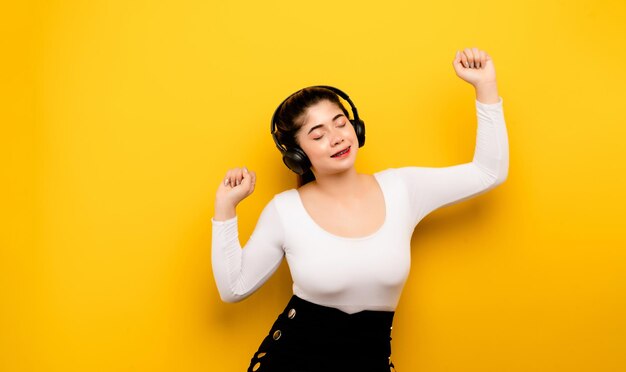 Woman listening to music A young woman wears headphones over her phone to listen to music via Bluetooth on a yellow background