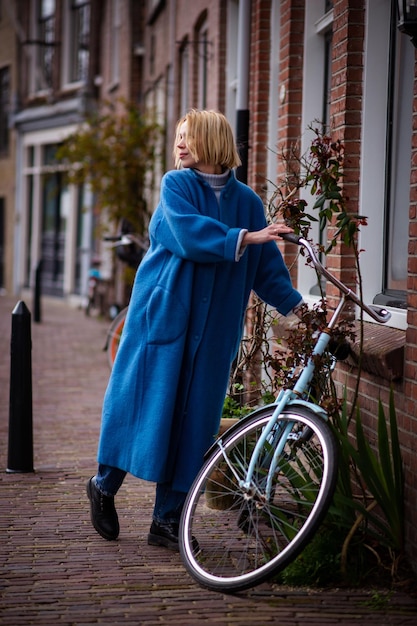 A woman in a long blue coat in the Netherlands Tourist while traveling in Rotterdam An adult woman takes a bicycle