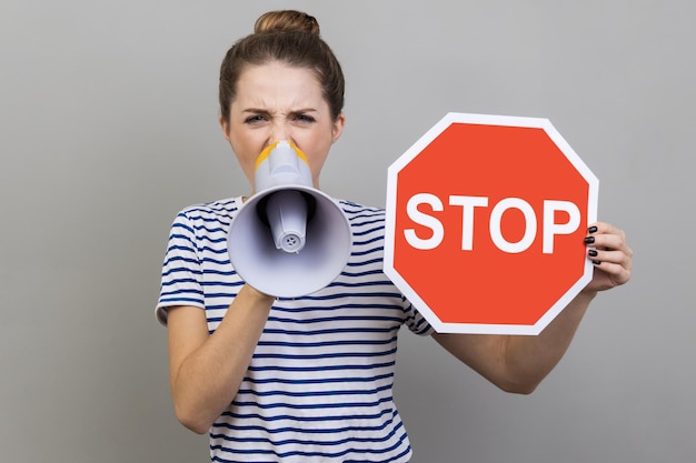 Woman looking at camera holding red stop sign and screaming in megaphone in her hands