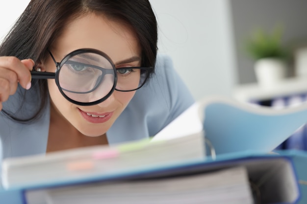 Woman looking at documents in folder through magnifying glass