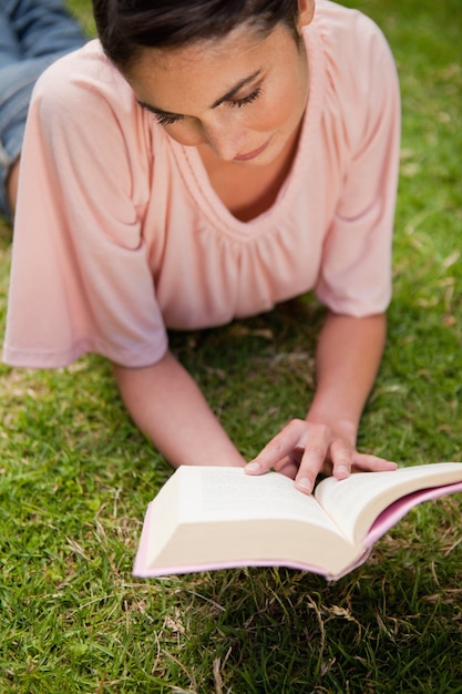 Woman looking down at a book while lying in grass