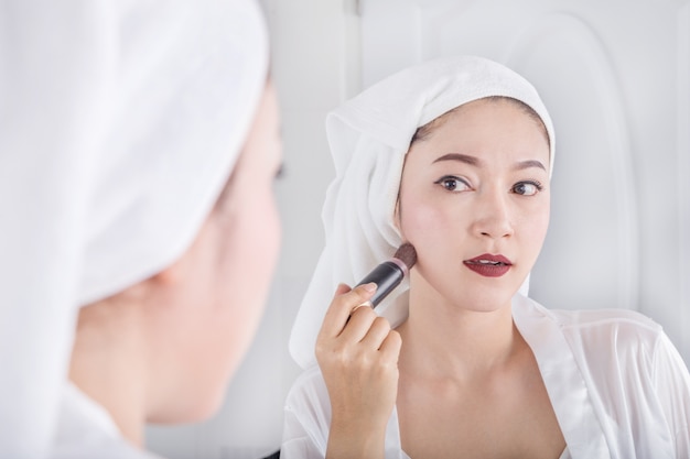 woman looking in the mirror and applying cosmetic with brush