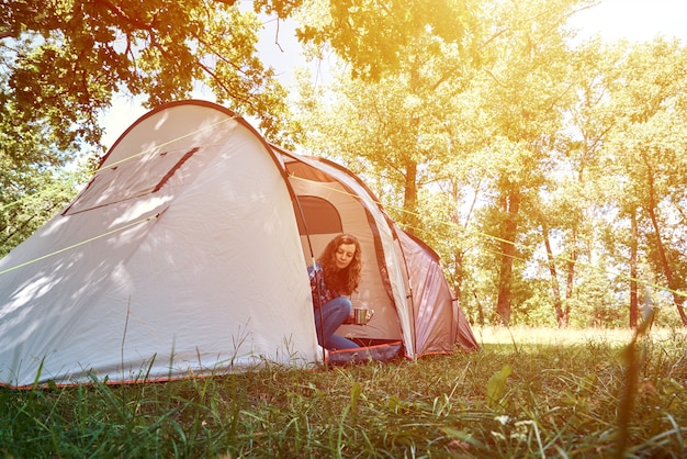 Woman looking out of tourist tent on sunny morning in forest