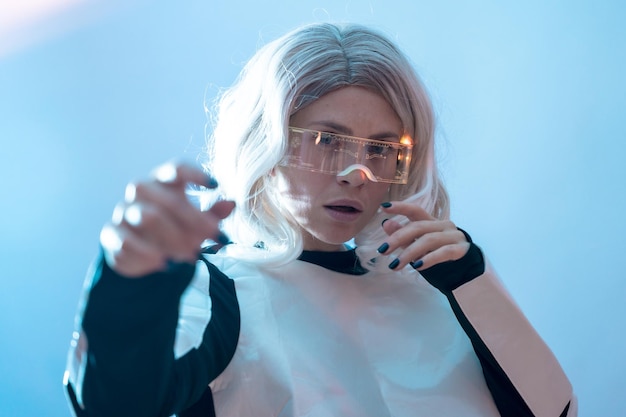 Woman looking through the illuminated futuristic glasses blue background enjoying virtual reality