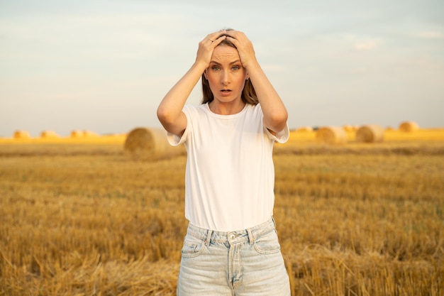 Woman looks fearfully into the camera against the background of a field with haystacks