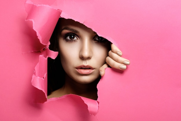 woman looks in hole colored pink paper, fashion beauty makeup and cosmetics, beauty salon