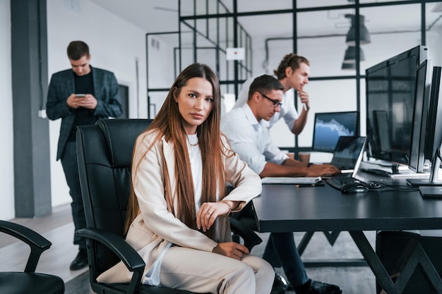 Woman looks into the camera Team of stockbrokers works in modern office with many display screens