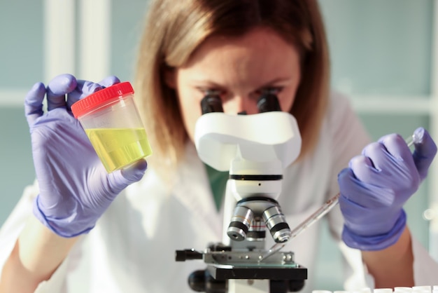 Woman looks into microscope laboratory assistant examines urine sample for analysis holding