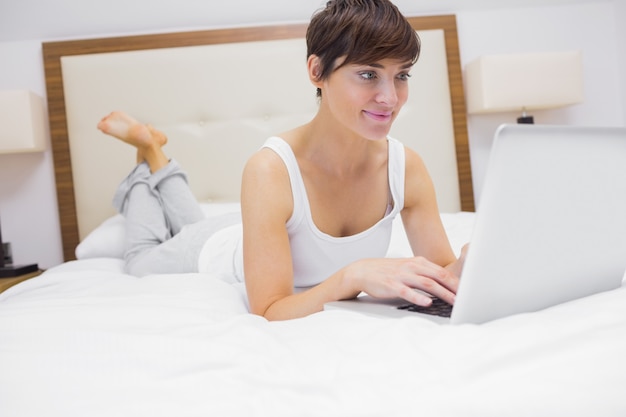 Woman lying on bed using laptop