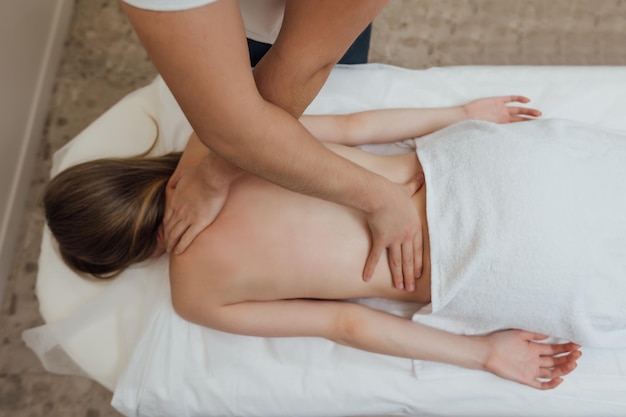 Woman lying face down on massage table and enjoying remedial body massage done by professional masseur in spa salon