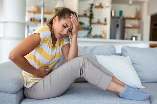 Woman lying on sofa looking sick in the living room Beautiful young woman lying on bed and holding hands on her stomach Woman having painful stomachache on bed Menstrual period