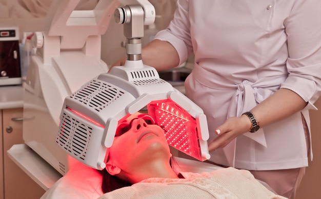 Woman lying on a table with protect glasses on eyes have a skin treatment under beauty device. Beauty spa salon.