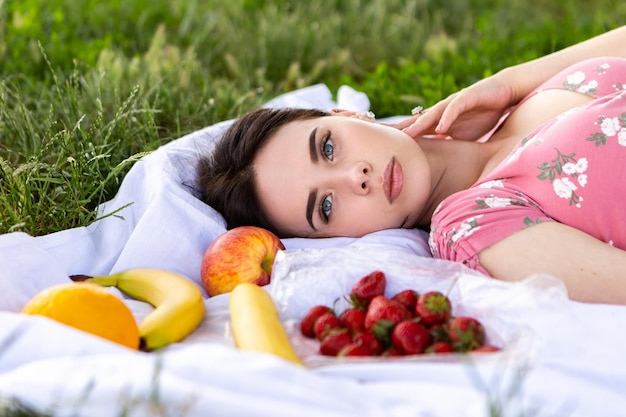 Woman lying on white bedsheet Lady have a rest in the city park green grass lawn A lot of fruits