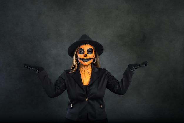 Woman made up as a pumpkin to celebrate Halloween pretending to hold something in her hands. Dark background with copy space.