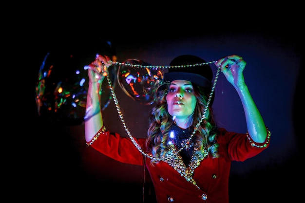 Woman magician illusionist circus with top hat in theatrical clothes shows soap bubbles show at black background Female actress