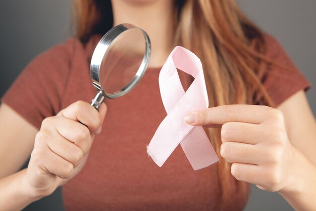 Woman magnifying glass looking at pink ribbon