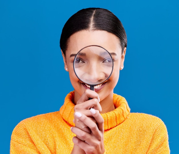 Woman magnifying glass and smile in studio portrait with funny face search and zoom by blue background Gen z girl investigation and research with lens for study inspection and check by backdrop