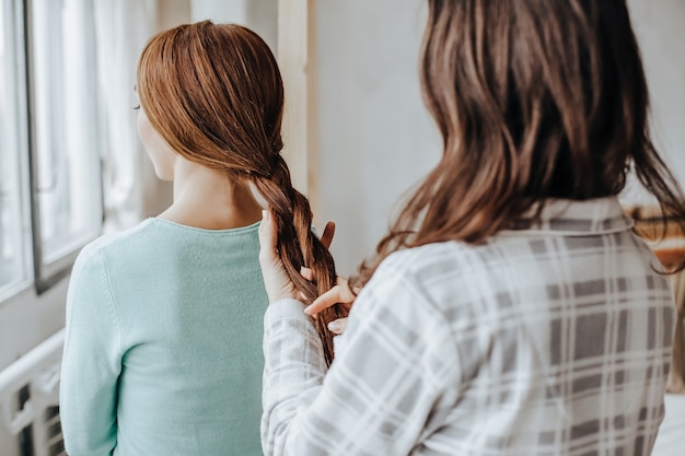 Woman makes a braid hair to her girl friend