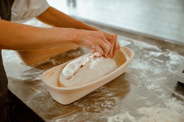 Woman makes decor on raw bread loaf in ceramic dish in craft bakery