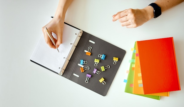 a woman makes a note in a notebook with scattered clips. Nearby is a stack of colored notebooks with bookmarks. High quality photo