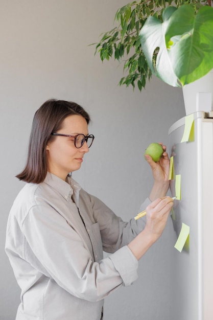 A woman makes notes on colored stickers on the refrigerator a reminder or a note for her husband and