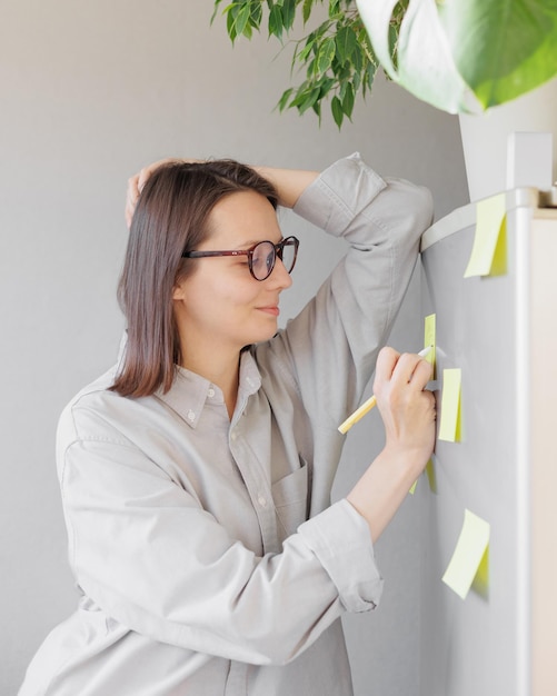 A woman makes notes on colored stickers on the refrigerator a reminder or a note for her husband and