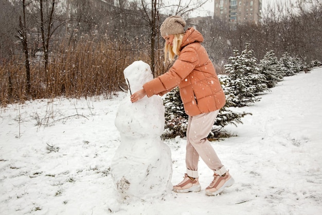 Woman makes a snowman in a city park during a snowfall