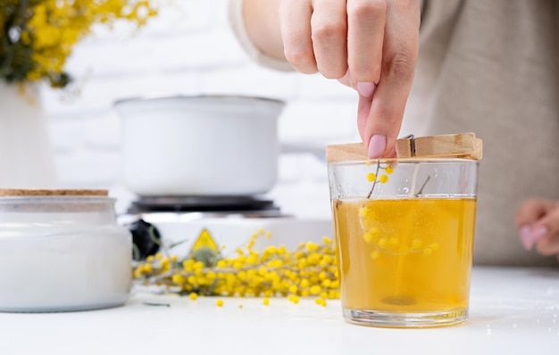 Woman making decorative aroma candle at table with mimosa closeup